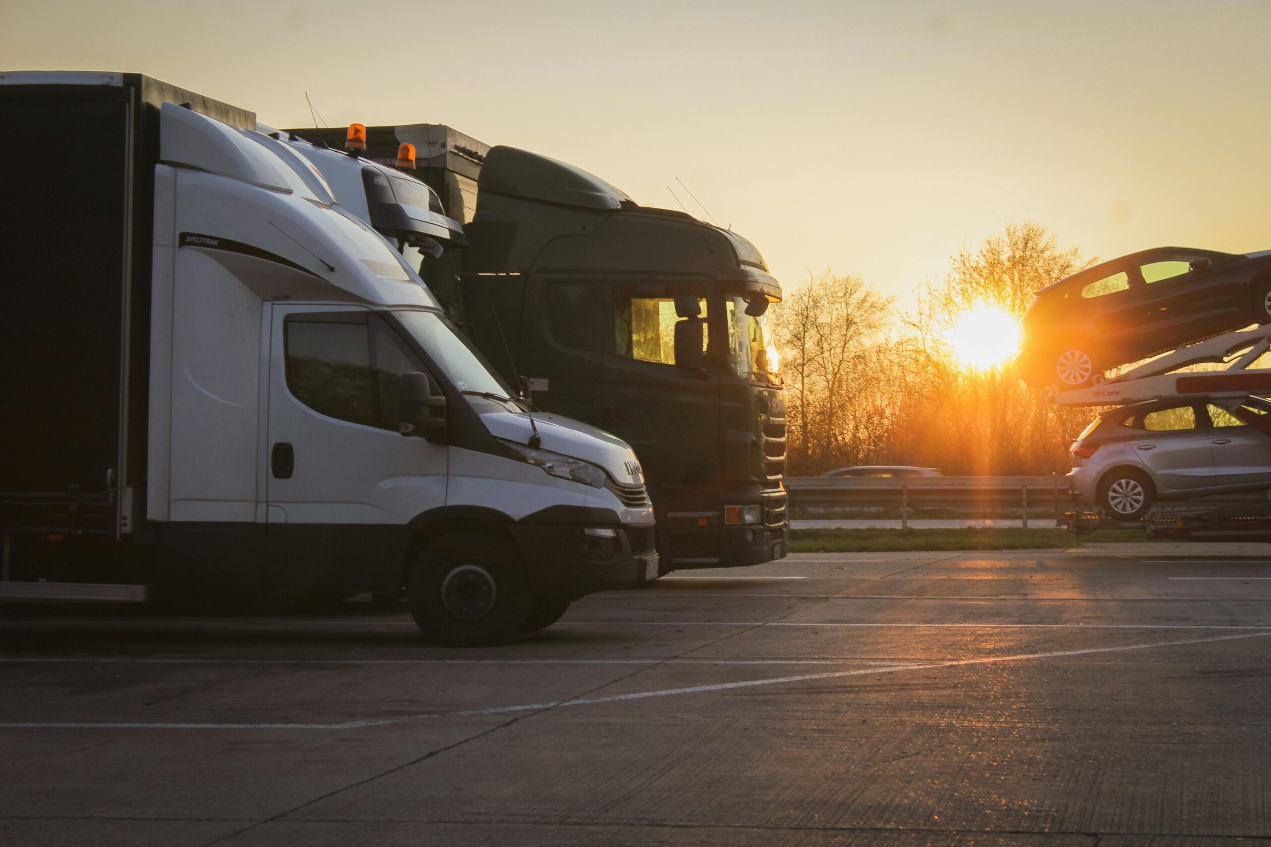 pexels-photo-1606957-1606957 A row of trucks and car transporter parked at sunset in an open parking lot, highlighting the golden hour.